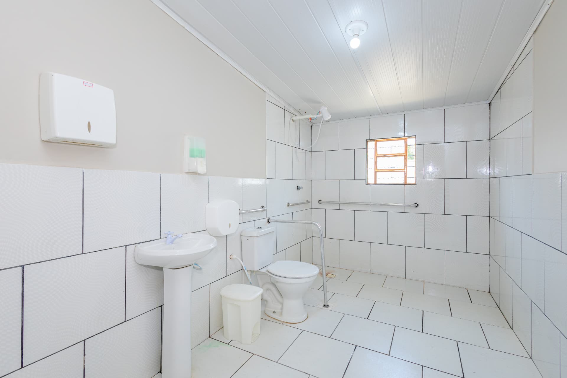 Banheiro amplo com barras de apoio junto ao vaso e ao chuveiro
