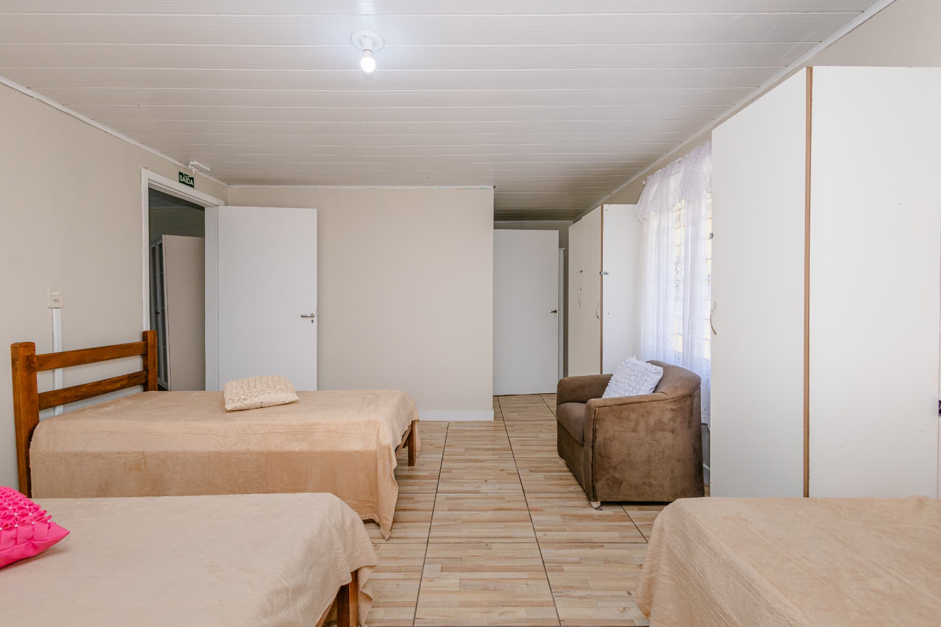 Quarto com três camas e poltrona junto ao armário