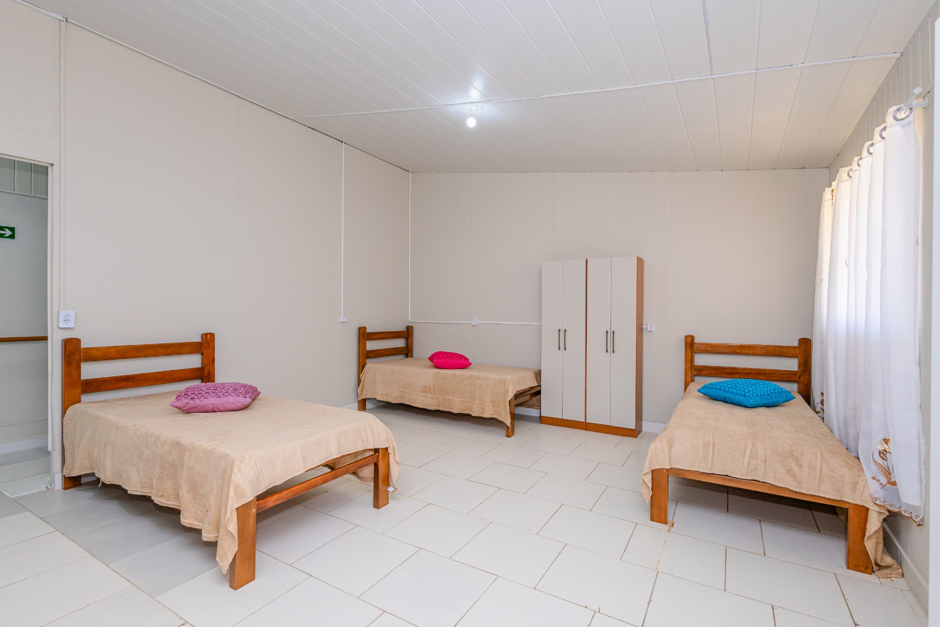 Dormitório com três camas individuais e guarda-roupa