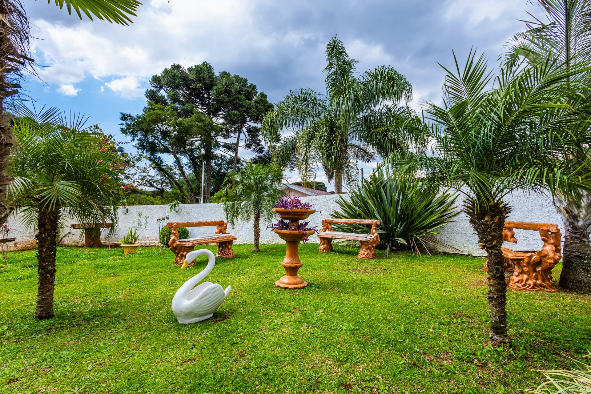 Jardim da casa, com bancos, palmeiras e canteiros