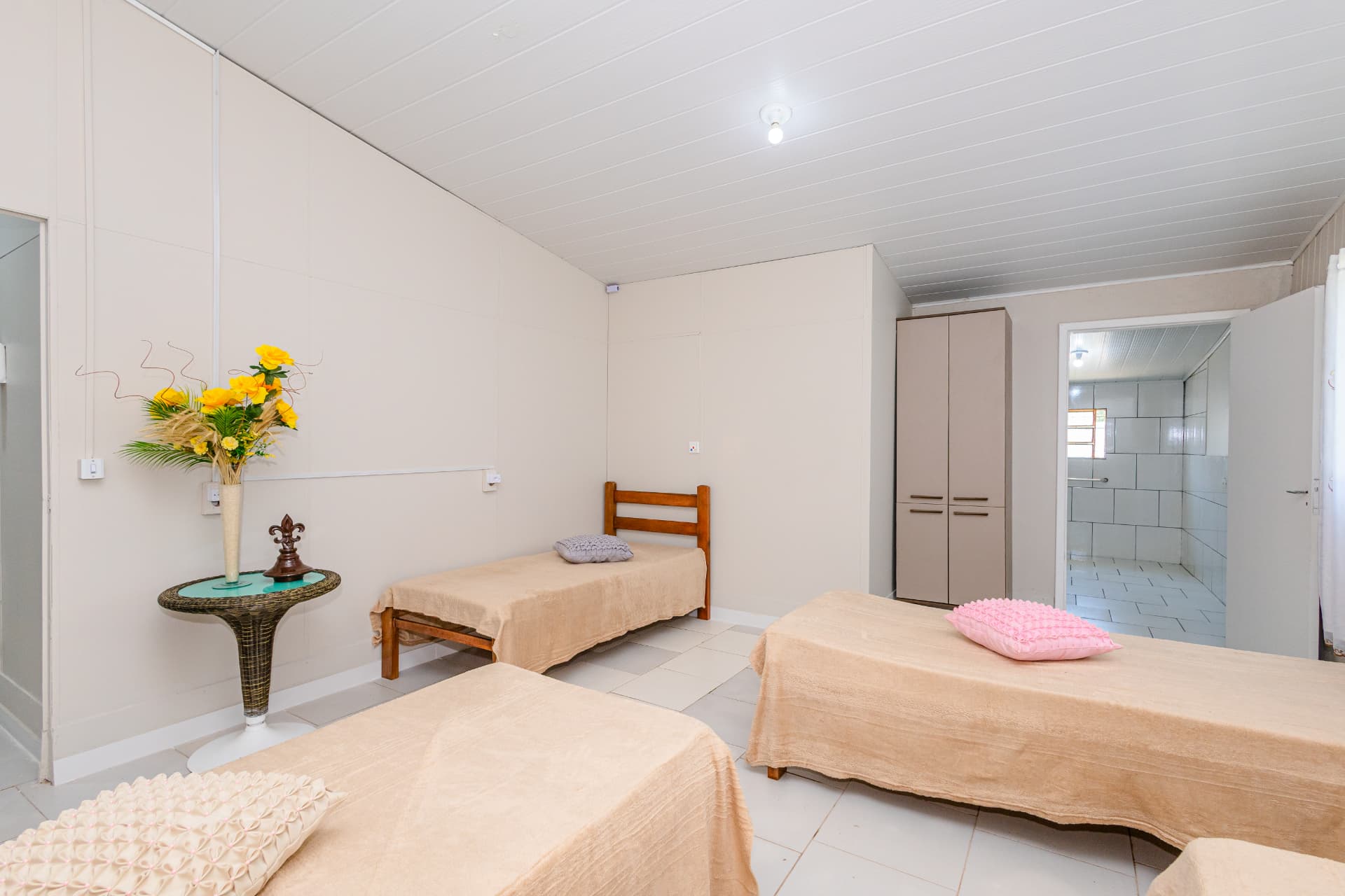 Quarto compartilhado com camas arrumadas e mesa lateral com flores